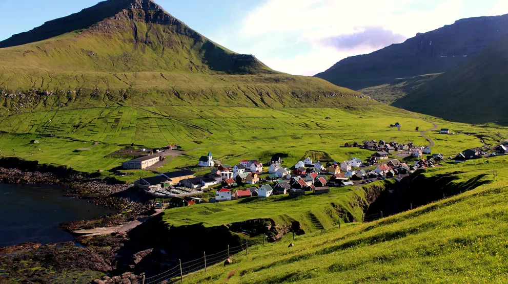 Gjogv ligger iddylisk placeret mellem de grønne bjerge - besøg den på rejsen til Færøerne