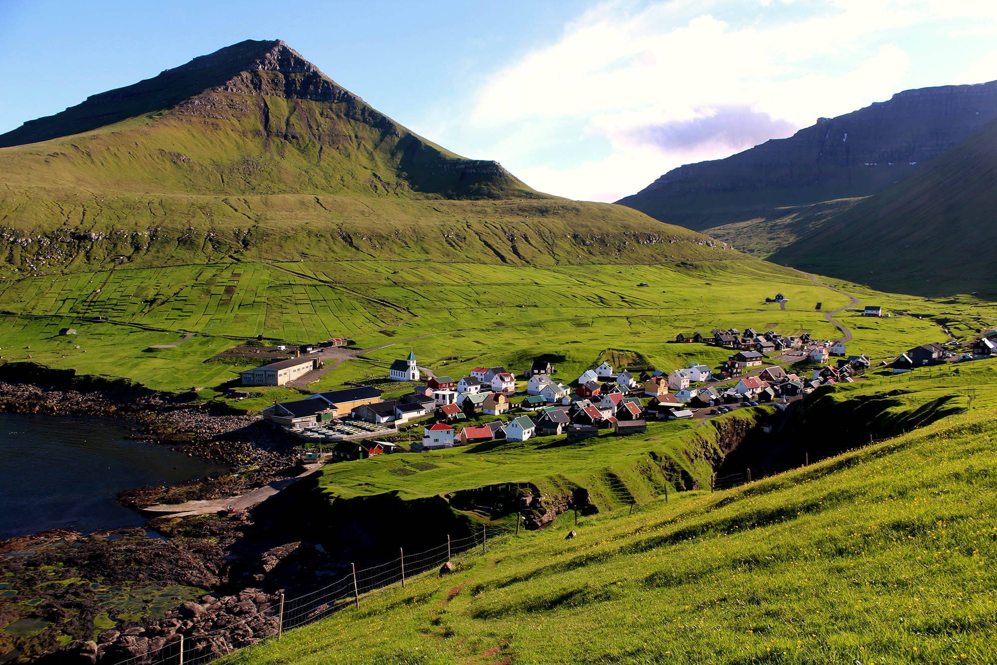 Gjogv ligger iddylisk placeret mellem de grønne bjerge - besøg den på rejsen til Færøerne